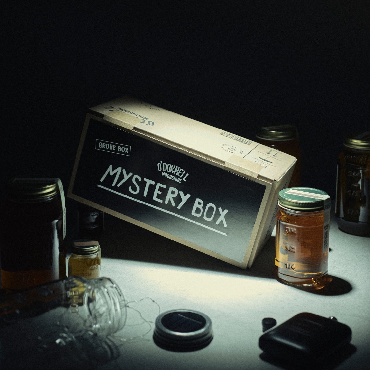 Ein Lifestyle-Bild der grosse Mystery Box. Die Mystery Box steht auf einem Tisch, umgeben von verschiedenen Gläsern und einigen Merchandise-Artikeln.