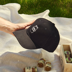 Eine männliche Hand hält O'Donnell Moonshine Black Cap mit einem kleinen Schnaps im Hintergrund, der auf einem Stück Stoff auf einer Wiese liegt