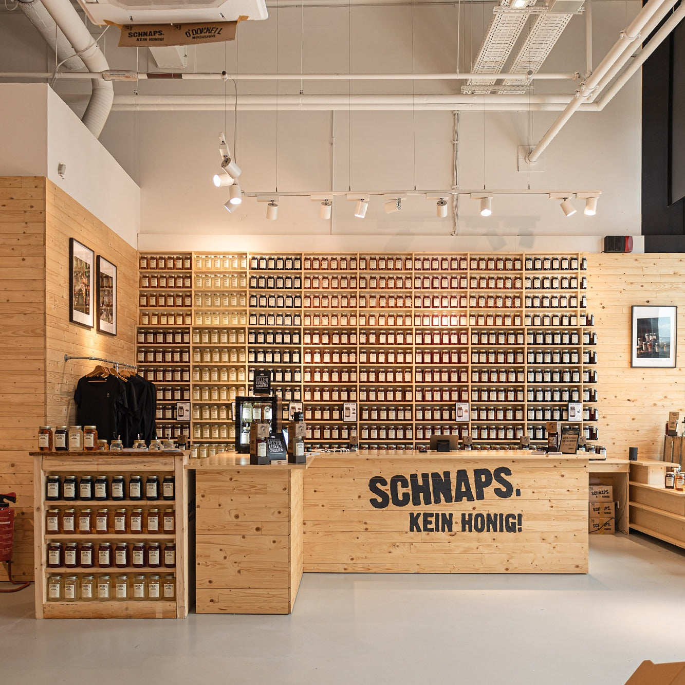Innenansicht des O'Donnell Moonshine Ladens in Bochum mit einer deckenhohen Regalwand voller Einmachgläser, einem hölzernen Verkaufstresen mit der Aufschrift „SCHNAPS. KEIN HONIG!“ und heller, industrieller Beleuchtung.