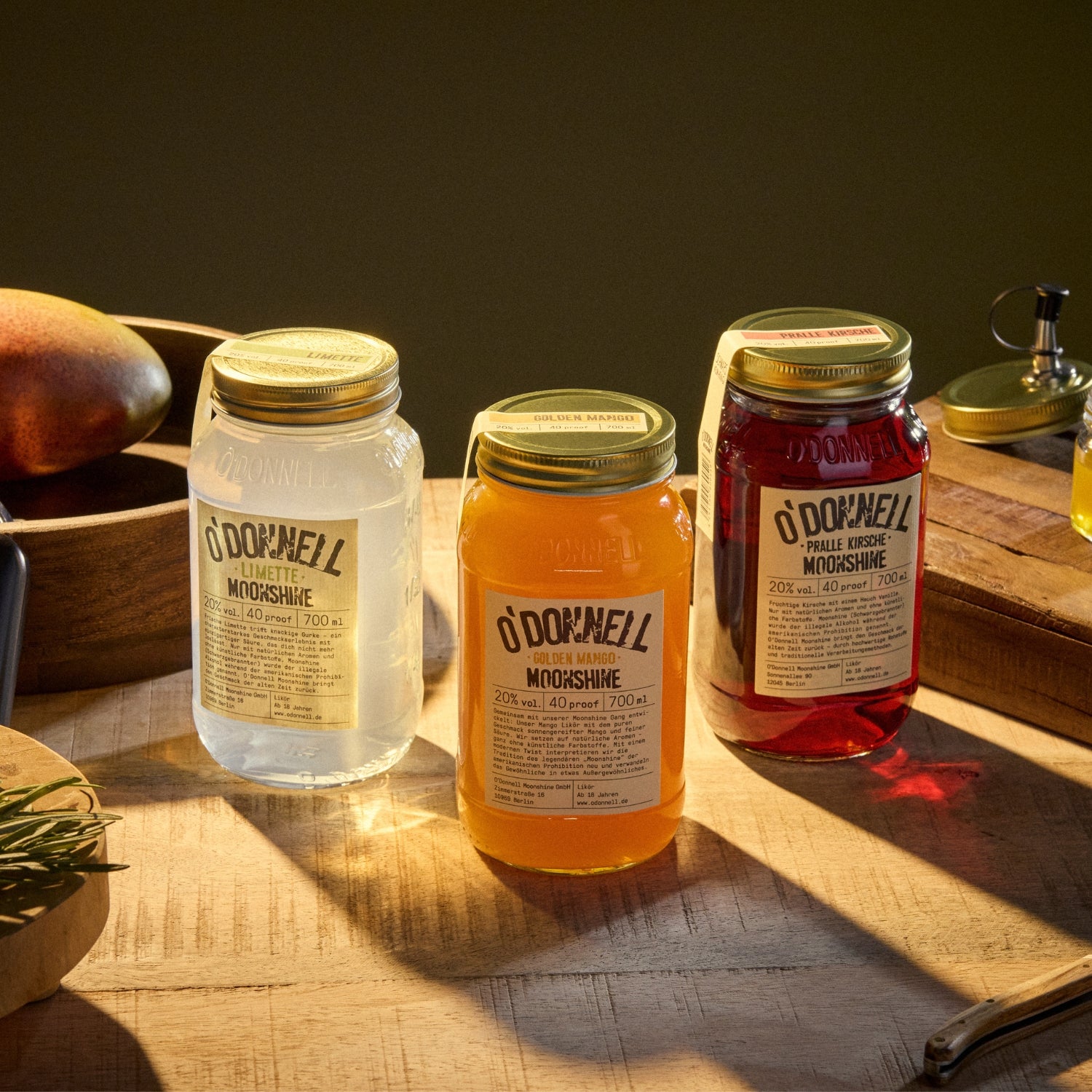 Drei Mason Jars von O'Donnell Moonshine in den Geschmacksrichtungen Limette, Golden Mango und Pralle Kirsche auf einem rustikalen Holztisch.