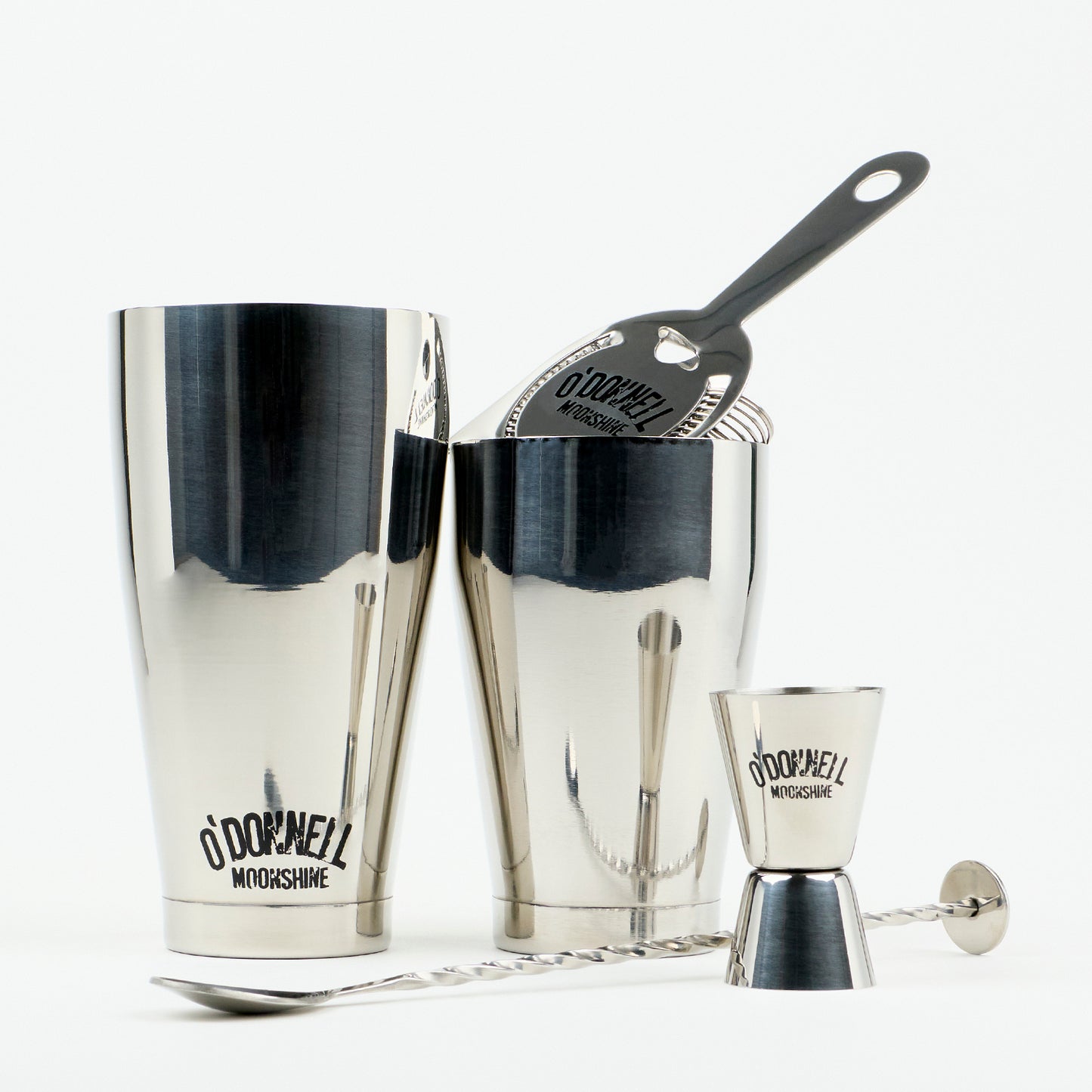 O'Donnell Moonshine Bar-Set aus Edelstahl mit Boston Shaker, Barsieb, Jigger und Barlöffel vor weißem Hintergrund.
